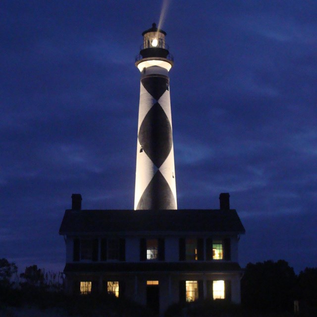 evening sky with black and white lighthouse behind a white colonial house