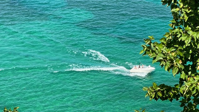 A motorized boat drives from the left side of the picture towards the right. The water is turquoise.