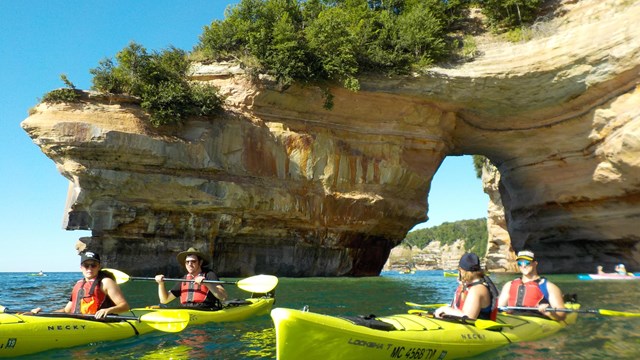 A group of people in three yellow kayaks with sandstone cliffs in the background.
