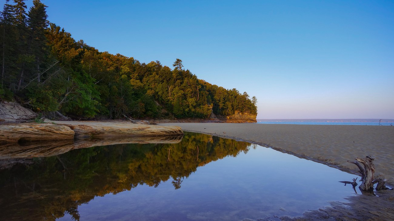 A calm river flows towards a sandstone cliff on a clear morning