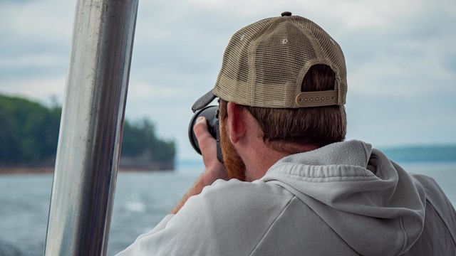 A person with their back to the camera takes a photo of the cliffs