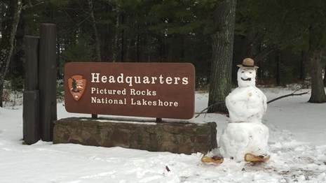 Wood park entrance sign mounted on stone base with a snow ranger next to it