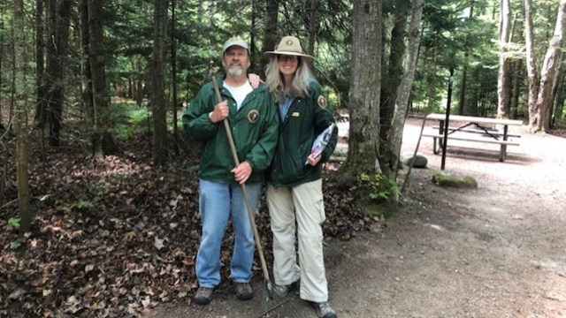 Two people wearing green jackets at a campground.