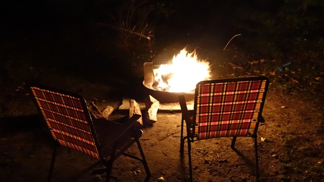 Two chairs sit around a firepit with a campfire at night.