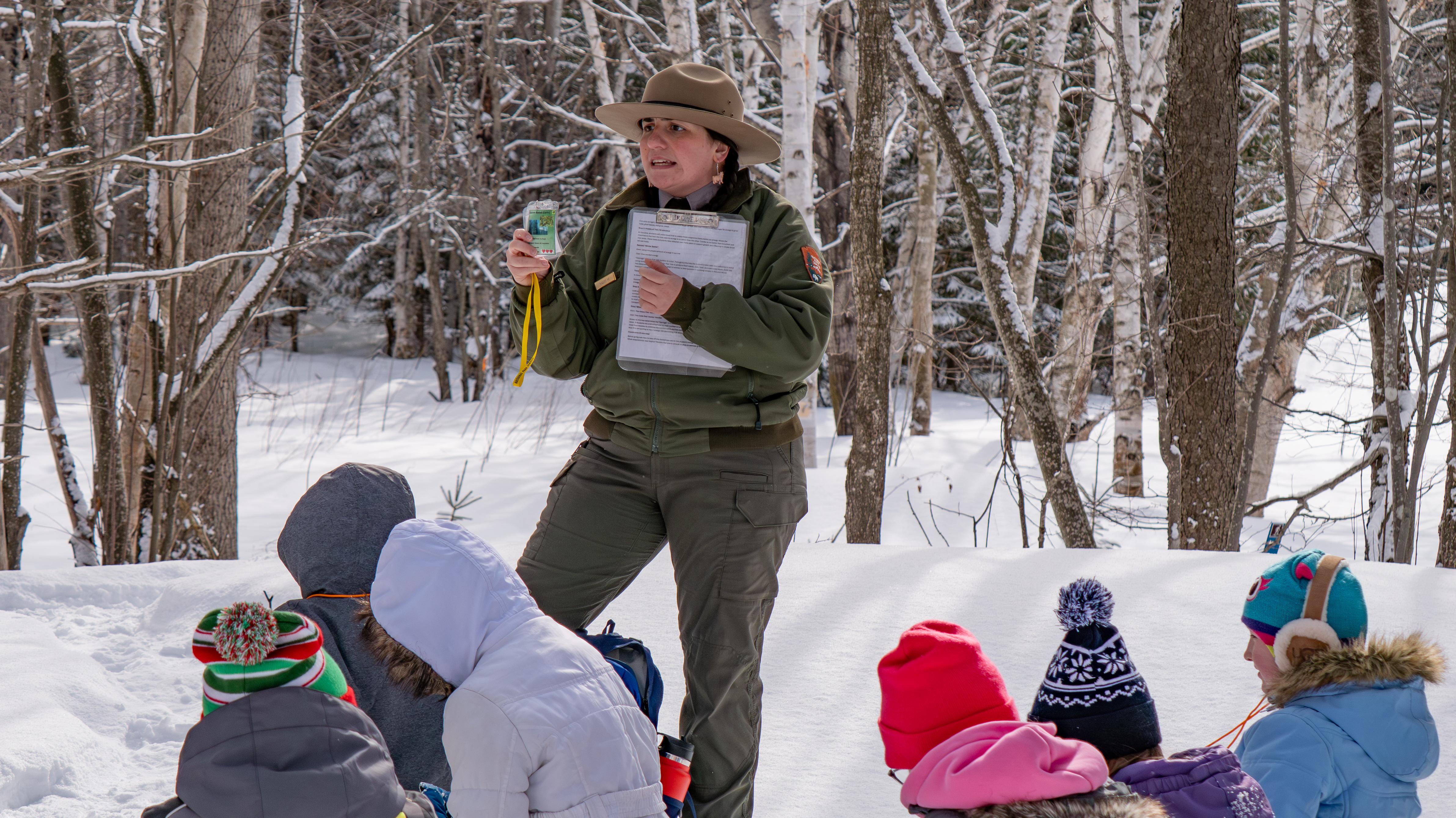 A ranger shows a photo to a group of school children on a wintry day.