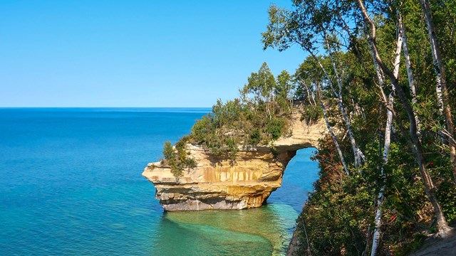 A sea arch rises out of a blue-green Lake Superior