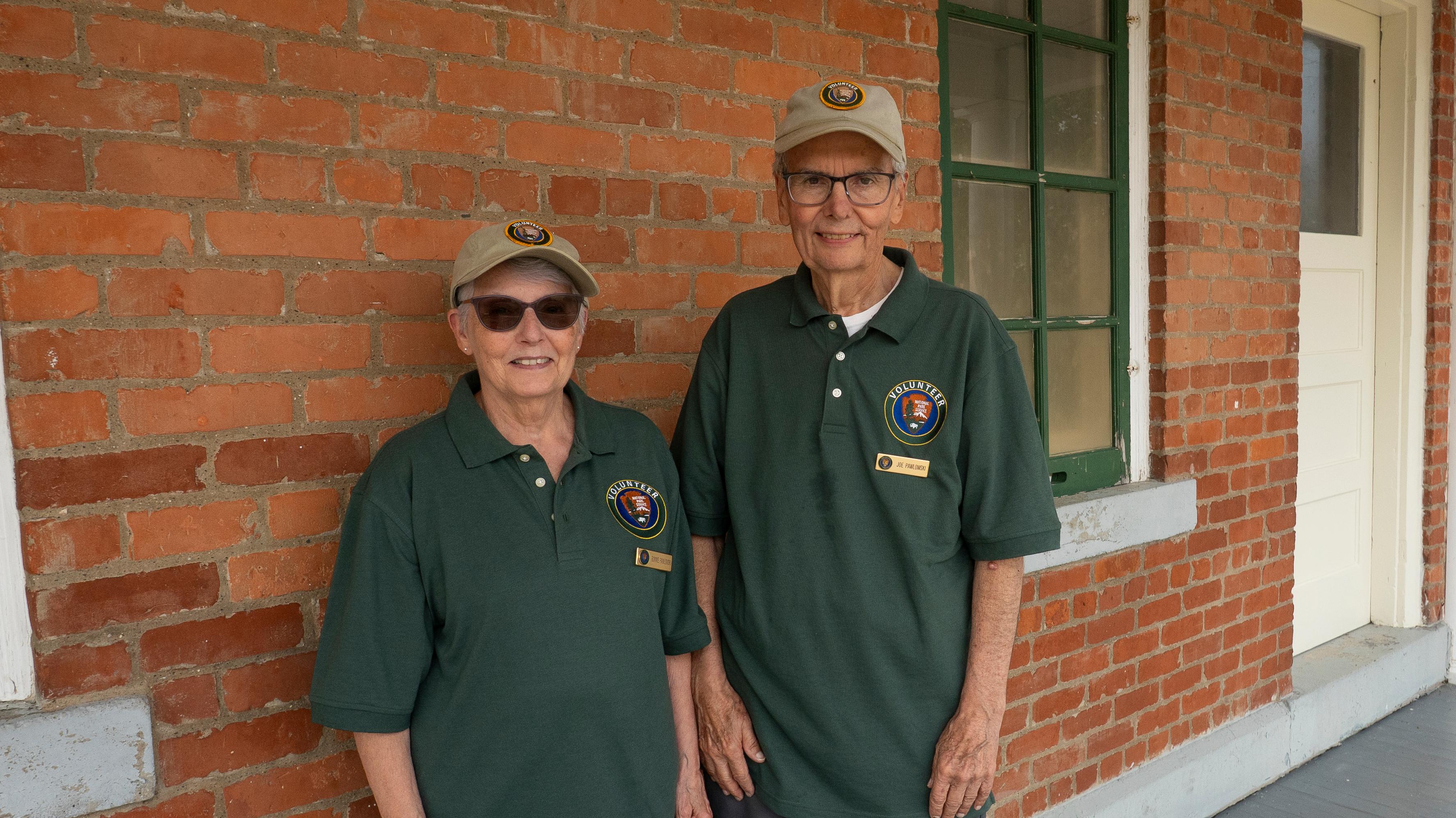 Two volunteers smile in front of a brick wall