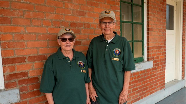 Two volunteers smile in front of a brick wall