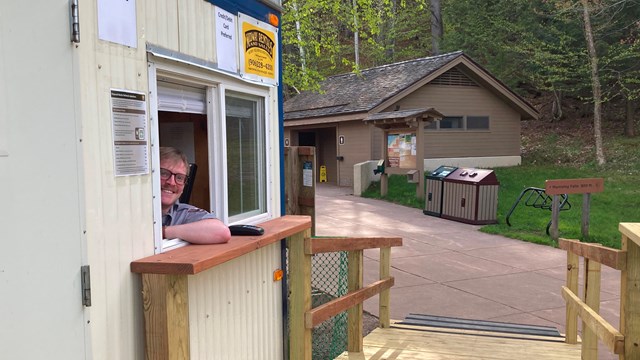 A ranger smiles from inside a fee collection booth.