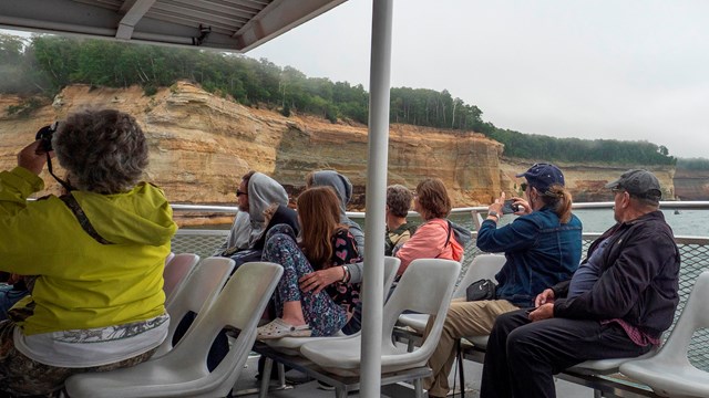 People take photos of the Pictured Rocks cliffs from a boat tour.