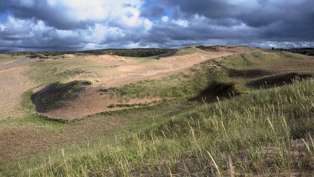 White and dark clouds over an expanse of open and grass-covered dunes.