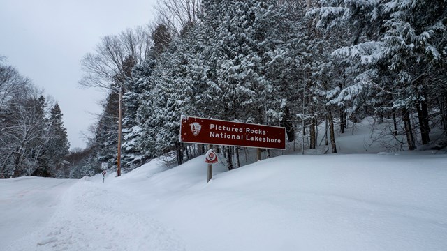 A sign reading "Pictured Rocks National Lakeshore" next to a snowy road.
