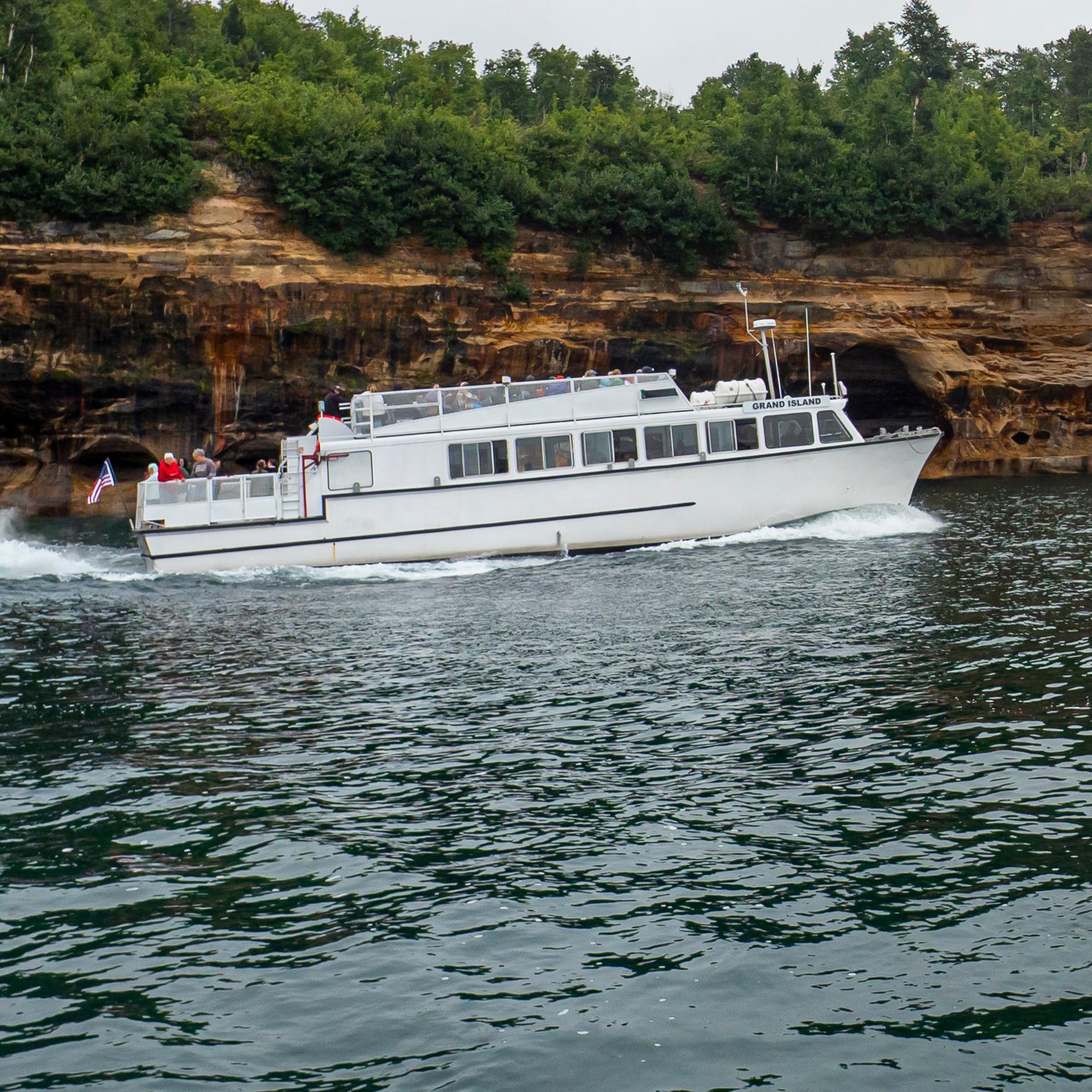 A white boat cruises by mineral-stained sandstone cliffs on a cloudy day.