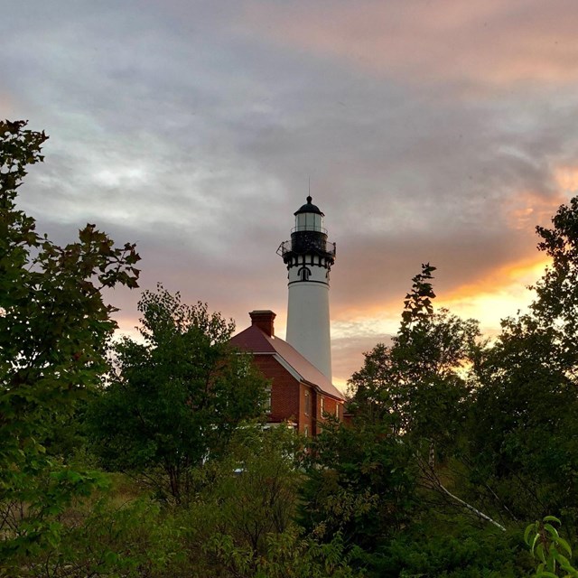 The Au Sable Light Station through shrubs and trees at sunset.