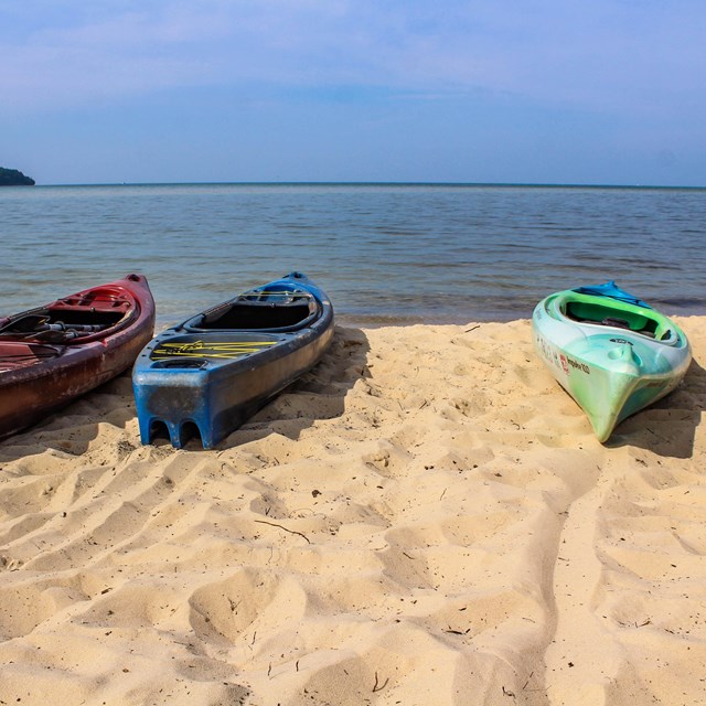 Three kayaks on a beach facing the water