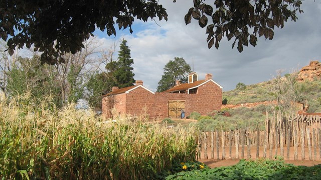 A sandstone fort, red cliffs, and garden plants in front of a baby-blue sky.