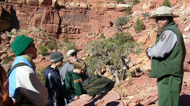 A Native American ranger leads hikers through a canyon with petroglyphs.