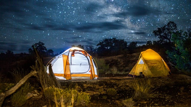 Two yellow tents lit up against nights sky