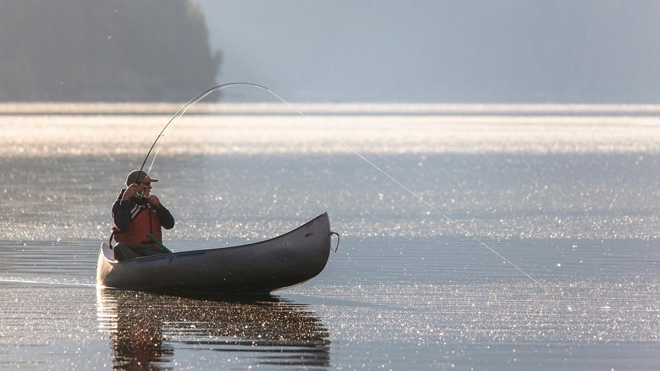Single person fishing by canoe on calm mountain lake