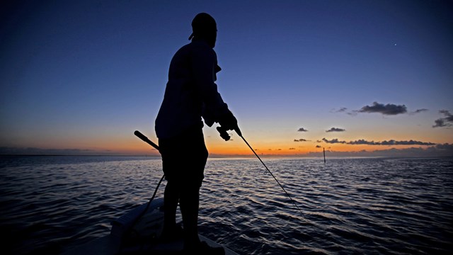 Silhouette of a person standing on a boat fishing at dusk