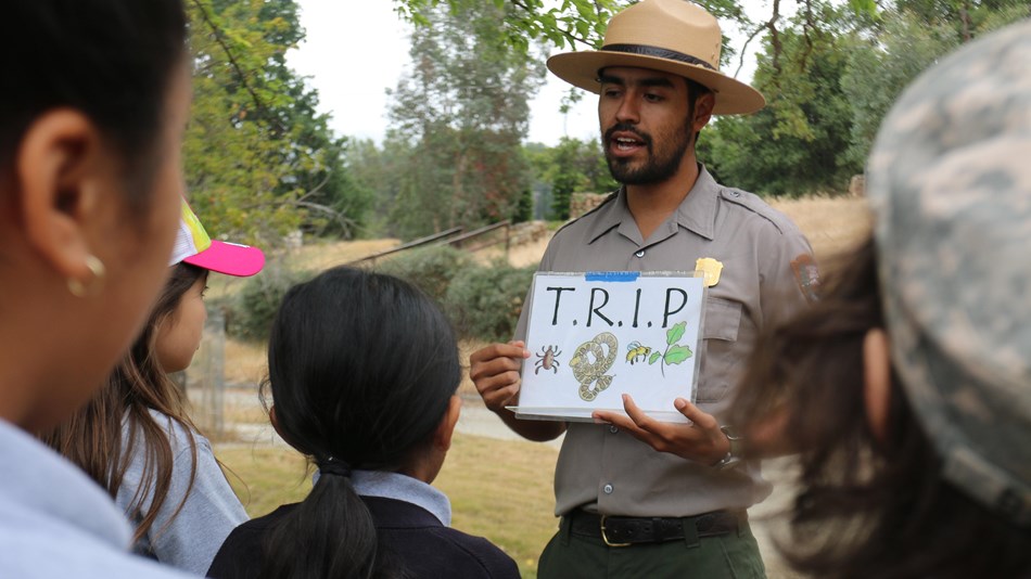 Park ranger talking to a group while holding a sign that reads 