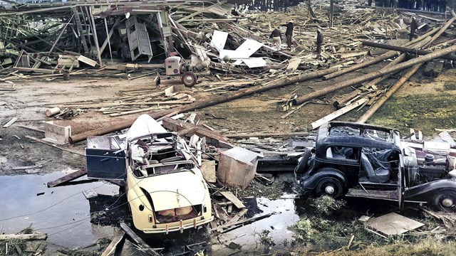 A colorized historic photo of the disaster aftermath which shows a lot of wooden debris and vehicles