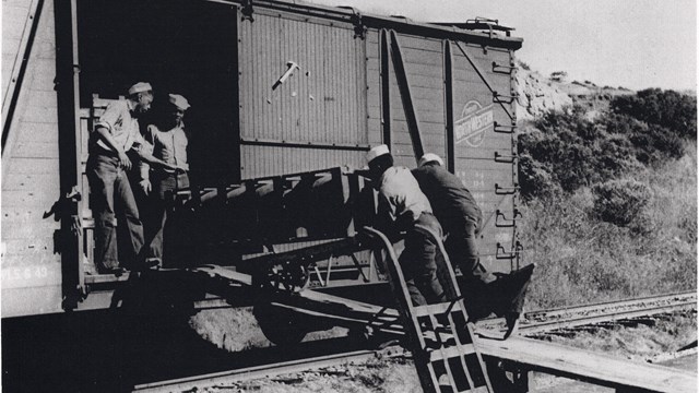 Historic photo of four African American sailors loading munitions into a box car. 