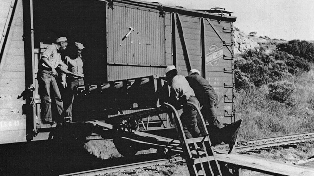 Four African American sailors load munitions into a boxcar.