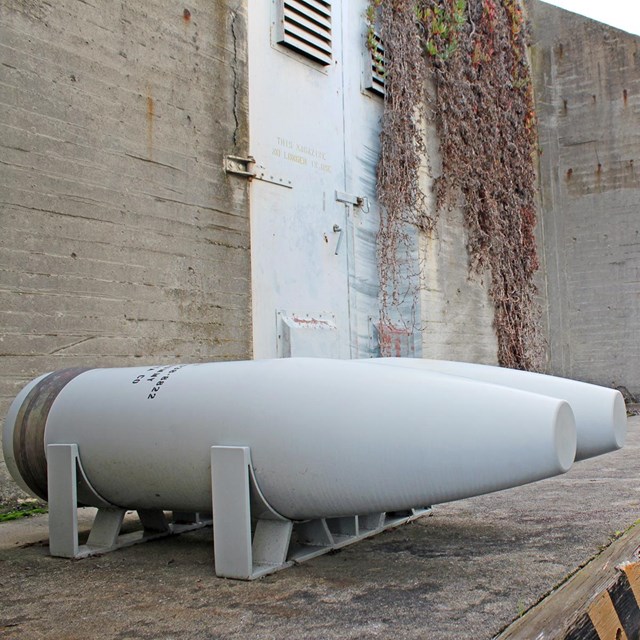 Two metal replica munition shells sit on a concrete wall inside the revetment. A male ranger. 