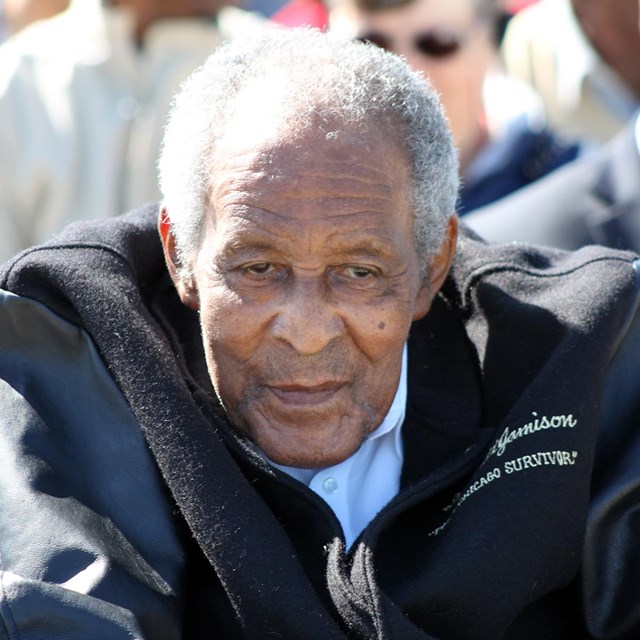 An elderly African American man in a jacket sits in a wheelchair. 