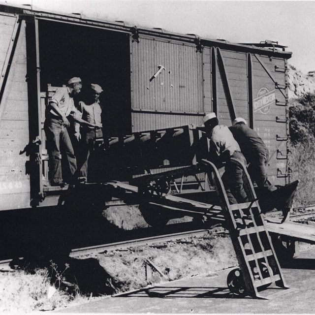 Historic photo of four African American sailors loading munitions into a box car. 