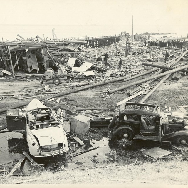 Historic photo of debris from the explosion. Two damaged vehicles in the forground. 