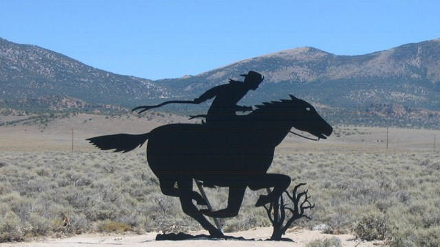 A silhouette image of a rider on a horse, in a desert setting.