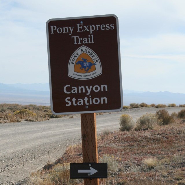 A brown sign with a pony express logo, next to a road.