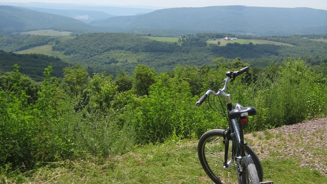 A bicycle standing overlooking a valley of rolling green hills and trees with smoky blue mountains.