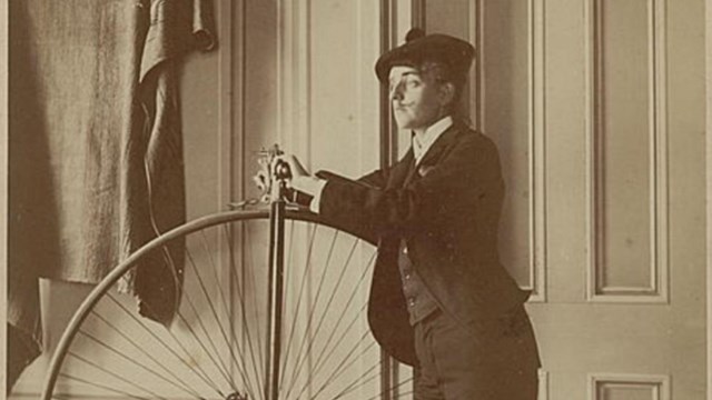 Woman humorously dressed as a man poses with a bicycle