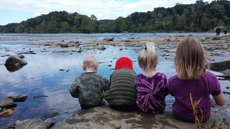 Four children sit on a rock along the water