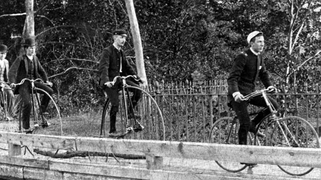 black and white photo of four men riding across a bridge 