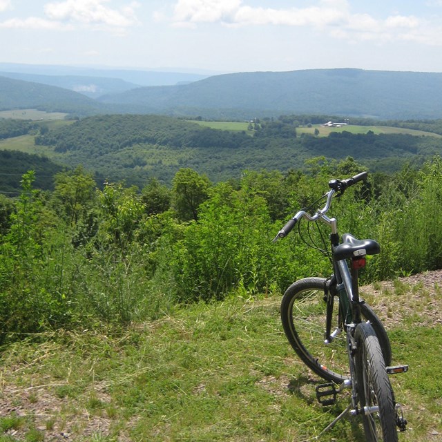 A bicycle standing overlooking a valley of rolling green hills and trees with smoky blue mountains.