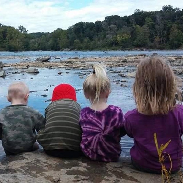 Four children sit on a rock along the water