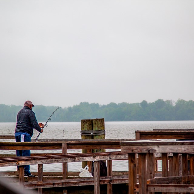 A person fishing on a pier by the water