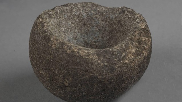 A semi-spherical brownish-gray granitic rock with a depression worn in on its top side.