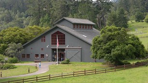 The Bear Valley Visitor Center. A gray, barn-like structure surrounded by oak and Douglas fir trees.