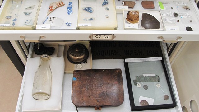 A museum cabinet with the contents of a couple drawers visible.