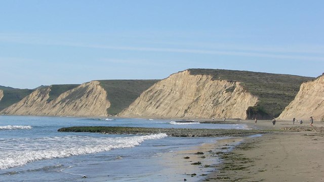 View looking across a beach with waves washing in from the left at the tan-colored bluffs.