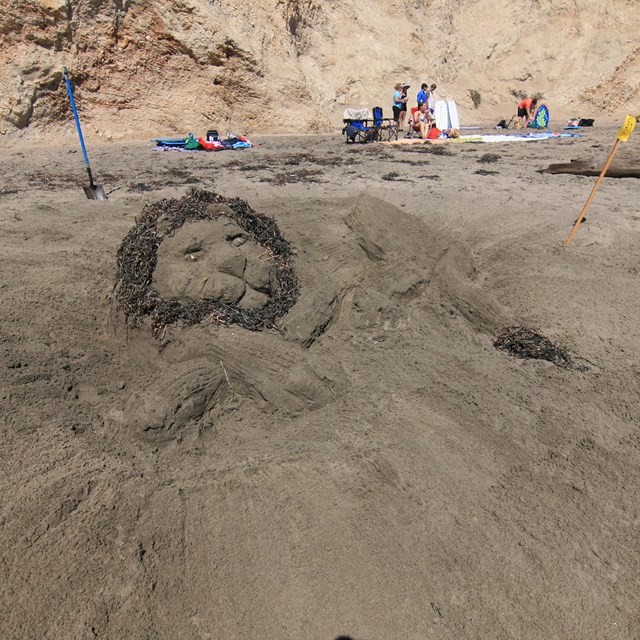 A sand sculpture of lion lying down with its head on its forepaws.