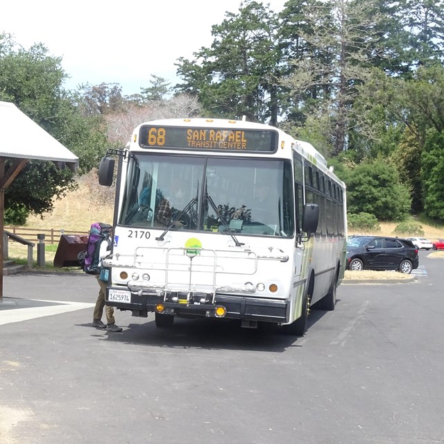 Two backpackers board a bus adjacent to a wooden bus stop.
