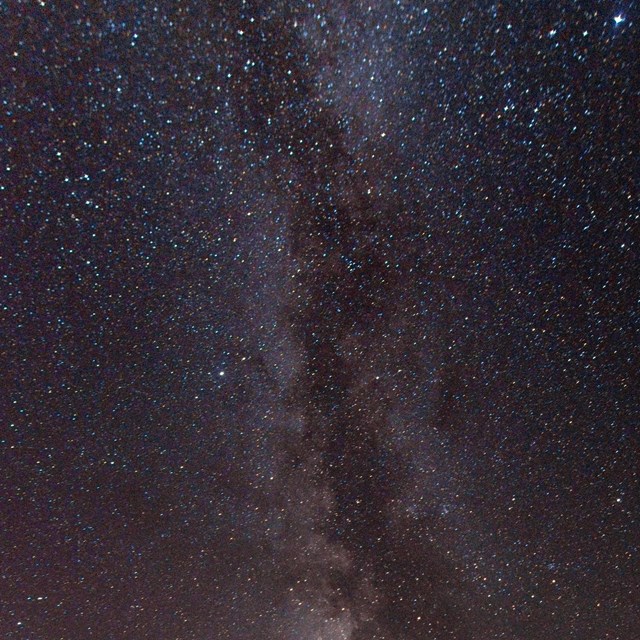 Hundreds of apparently tiny stars and the Milky Way against the dark night sky.