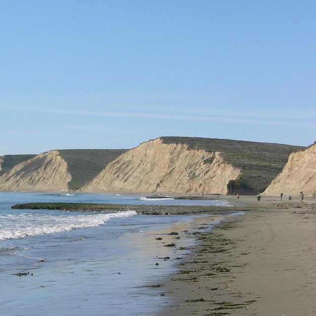 View looking across a beach with waves washing in from the left at the tan-colored bluffs.