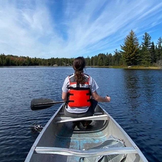 A person in a lifejacket sits in a canoe on a lake